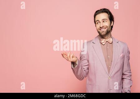 Junger Veranstaltungsort in Jacke und Fliege mit isoliertem Finger auf pinkfarbenem Stockbild Stockfoto