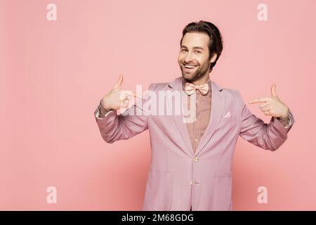Positiver Veranstaltungsort in der Jacke, der mit den Fingern auf pinkfarbenen Hintergrund zeigt, Stockbild Stockfoto