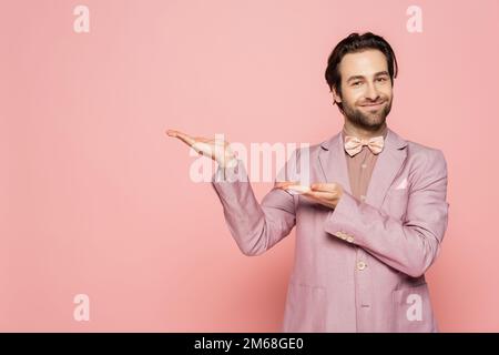 Positiver Veranstaltungsort in Jacke und Fliege mit Händen auf rosa Hintergrund, Stockbild Stockfoto