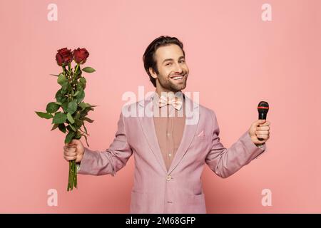 Stilvoller Veranstaltungsort mit Jacke und Fliege mit Mikrofon und Blumen auf pinkfarbenem Hintergrund, Stockbild Stockfoto
