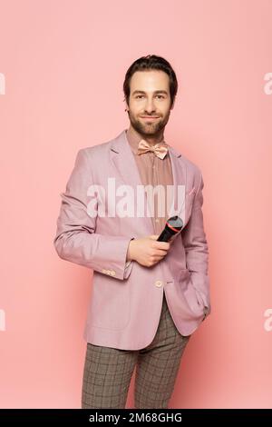 Porträt des Veranstaltungsorts in Fliege und Jacke mit Mikrofon isoliert auf pinkfarbenem Stockbild Stockfoto