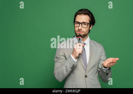 Brünette Nachrichtensprecherin mit Brille, die vor dem Mikrofon auf grünem Hintergrund spricht, Stock Image Stockfoto