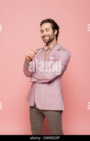 Lächelnder Veranstaltungsort in Jacke und Fliege mit Blick auf die Kamera auf pinkfarbenem Hintergrund, Stockbild Stockfoto