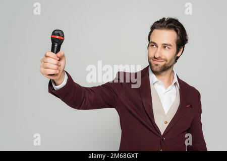 Fröhlicher Veranstaltungsort in formeller Kleidung mit Blick auf das Mikrofon isoliert auf grauem Stockbild Stockfoto