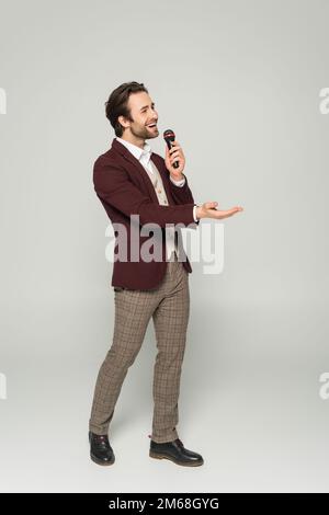 Ein bärtiger Showman in formeller Kleidung singt in einem Mikrofon auf grauem Stockbild Stockfoto