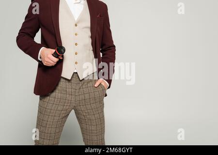 Zugeschnittene Ansicht des Showmans in formeller Kleidung, der mit der Hand in der Tasche steht und das Mikrofon hält, isoliert auf grauem Stockbild Stockfoto