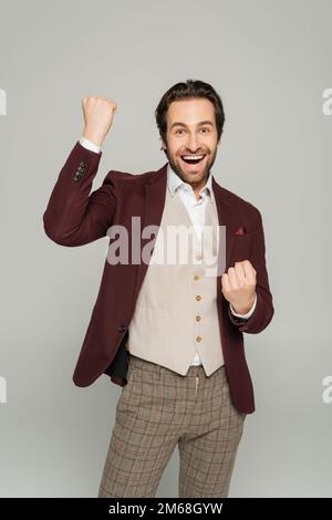 Begeisterter Showman in rotem Blazer Gesten, während er sich auf einem grauen, bunten Bild freut Stockfoto