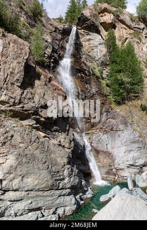 Wasserströme strömen über Granitstromschnellen in den smaragdgrünen See, den sie unten bildeten, und wenige Bäume auf umliegenden Felsen. Aosta Valley, Italien (vertikale Aufnahme) Stockfoto