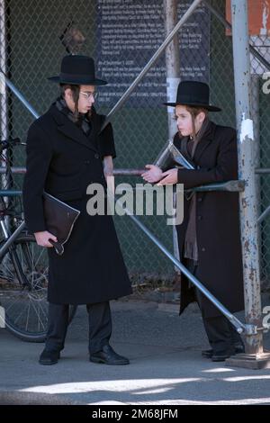 Chassidische Teenager mit einem langgewellten Peyot unterhalten sich nach dem morgendlichen Gottesdienst. In Brooklyn, New York. Stockfoto