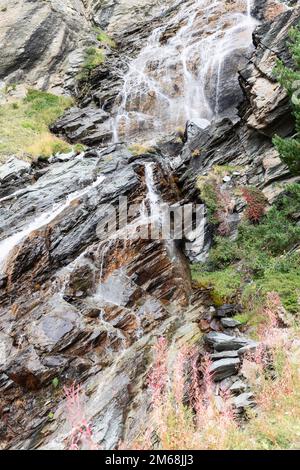 Spärliche Herbstvegetation von Moosen, Flechten und Gräsern verschiedener Arten, Farben und Schattierungen auf braunen Karstgranitfelsen und fließendem schaumigen Wasser von A Stockfoto