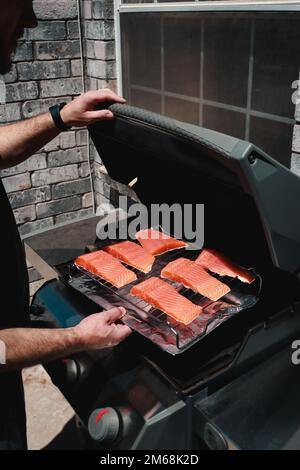 Nahaufnahme eines Mannes, der frische Lachssteaks auf den Grill legt Stockfoto
