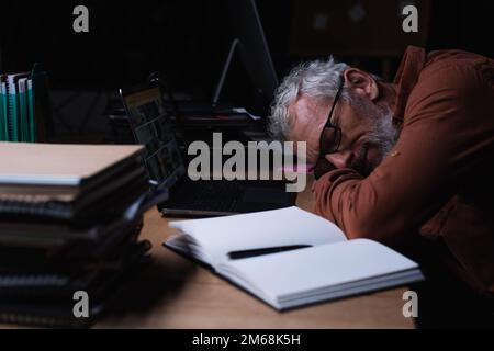 Erschöpfter Geschäftsmann, der nachts in der Nähe von Notebook und Laptop im Büro schläft, Bild der Aktien Stockfoto