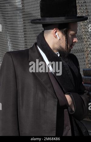 Ein chassidischer jude vermischt Tradition mit Technologie und trägt sowohl Peyus als auch AirPods. Bei einem Pop-up-Buchverkauf in Brooklyn, New York, Ende 2022. Stockfoto