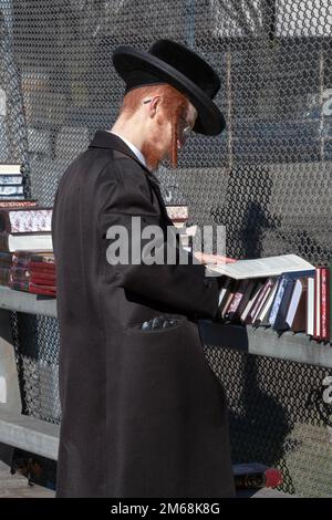 Ein ultraorthodoxer jüdischer Mann mit rotem Bart und roten Peyot-Shops für Bücher an einem milden Wintersonntag. In Brooklyn, New York City. Stockfoto