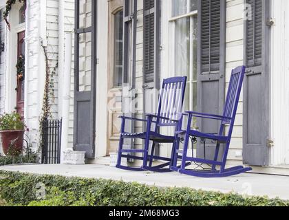 Zwei blaue Schaukelstühle aus Holz auf der Veranda eines Hauses im südlichen Kolonialstil der USA mit grauen Fensterläden an den Fenstern und Klappbrettern Stockfoto