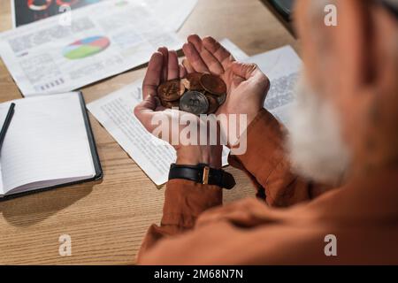 KIEW, UKRAINE - 17. NOVEMBER 2022: Teilweise Sicht auf reife Geschäfte mit einer Handvoll Bitcoins in der Nähe von leeren Notizbüchern und Dokumenten im Büro Stockfoto