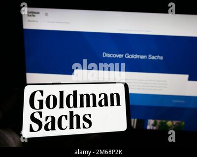 Person, die eine Handynummer mit dem Logo des amerikanischen Finanzunternehmens Goldman Sachs Group Inc. Auf dem Bildschirm vor der Webseite hält. Konzentrieren Sie sich auf das Display des Telefons. Stockfoto