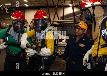 PHILIPPINISCHE SEE (19. April 2022) Seeleute üben die Brandbekämpfung während einer allgemeinen Quartierübung in der Hangarbucht an Bord des Flugzeugträgers USS Abraham Lincoln (CVN 72) der Nimitz-Klasse. Die Abraham Lincoln Strike Group befindet sich in einem geplanten Einsatz im US-7.-Flottenbereich, um die Interoperabilität durch Allianzen und Partnerschaften zu verbessern und gleichzeitig als einsatzbereite Truppe zur Unterstützung einer freien und offenen Region Indo-Pacific zu fungieren. Stockfoto