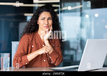 Büroangestellte im Büro haben schlimme Zahnschmerzen, lateinamerikanische Geschäftsfrau bei der Arbeit, die ein Notebook benutzt. Stockfoto