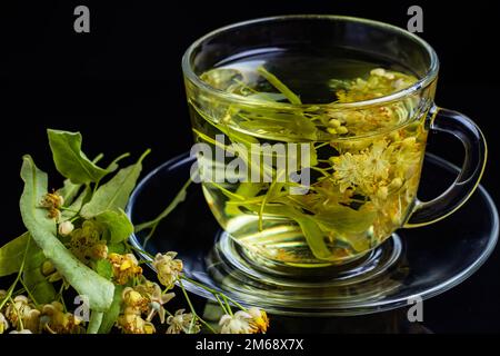Eine Tasse Kräutertee mit Lindenblumen auf schwarzem Hintergrund. Stockfoto