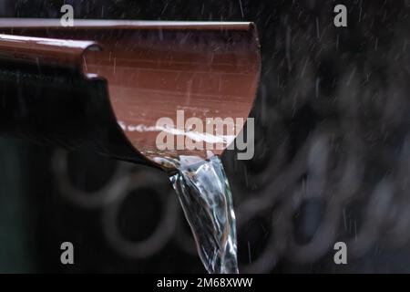 Regenwasser strömt aus der grünen Abflussrinne auf dem Gehweg, selektiver Fokus Stockfoto