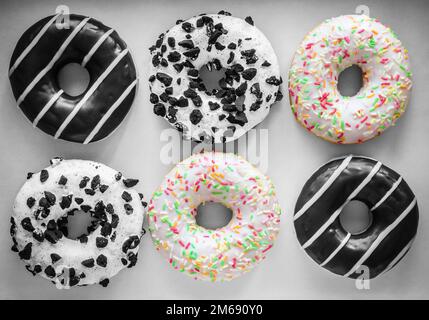 Flach legen Bild von sechs Ring Donuts mit weißer Glasur und bunten Hunderte und Tausende, Schokolade und Streifen und weiße Glasur mit schwarzen Cookies, bla Stockfoto