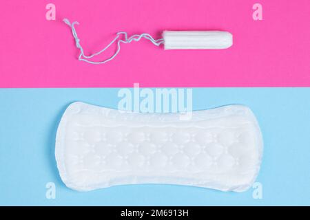 Damenpolster und Tampon – Hygienepads liegen neben einem Tampon auf einem isolierten Hintergrund auf einem pinkfarbenen und blauen Hintergrund. Frauenhygiene und Menstruation per Stockfoto