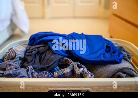 Ein Korb mit sauberer Wäsche im Schlafzimmer. Zufällige Anordnung von Kleidern im Korb sieht unordentlich aus. Stockfoto