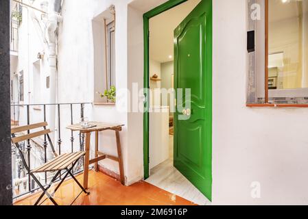 Kleine Terrasse mit einem zusammenklappbaren Holztisch mit passendem Stuhl neben einer grünen Eingangstür Stockfoto