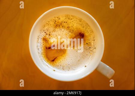 Eine Tasse Kaffee auf einem Tisch, von oben gesehen. Café Latte Macchiato mit Kaffeeflecken auf dem Getränk und Blasen im Schaum. Stockfoto
