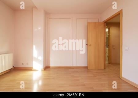 Leeres Zimmer mit weißen Holztüren, zwei eingebauten Kleiderschränken, heller Holztür und Laminatboden Stockfoto