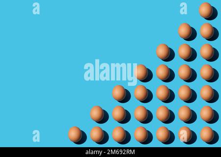 Ein Muster brauner Hühnereier, die diagonal in der unteren rechten Hälfte des blauen Hintergrunds liegen. Flach liegend, Kopierbereich. Stockfoto