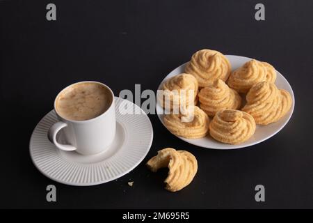 Baiser-Fotokuchen auf einem weißen Teller und eine Kaffeetasse mit Kaffee auf schwarzem Hintergrund Stockfoto