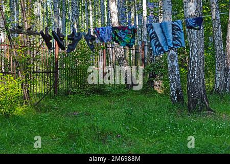 Flip-Flops hängen und trocknen an einem Seil, das sich zwischen Bäumen erstreckt. Stockfoto