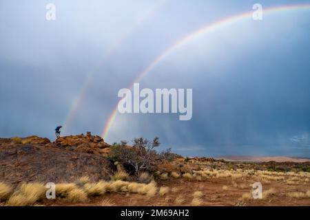 Ein doppelter Regenbogen und Sturmwolken über felsigen Felsvorsprüngen. Augrabies Falls-Nationalpark, Südafrika. Stockfoto