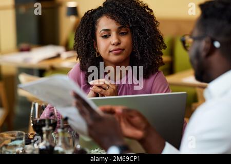 Eine fokussierte Geschäftsfrau sitzt mit ihrem Kollegen in einem Restaurant und hört sich Ratschläge für ein Start-up-Unternehmen an. Stockfoto