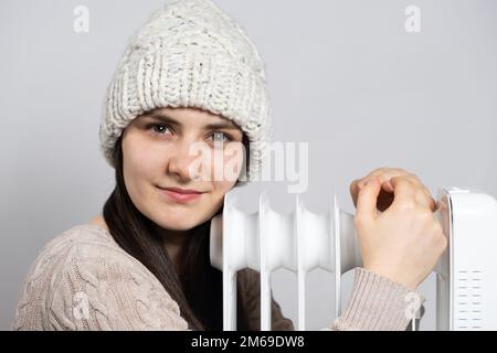 Eine brünette Frau mit Hut umarmt einen Ölwärmer und wärmt sich im Winter auf. Stockfoto