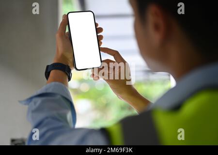 Ingenieur, der ein Smartphone benutzt, während er auf der Baustelle steht. Ansicht über Schulter Stockfoto