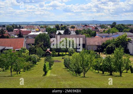 Österreich, Blick auf ein kleines Dorf in ländlicher Umgebung mit einem kleinen Obstgarten und Windturbinen im Hintergrund Stockfoto