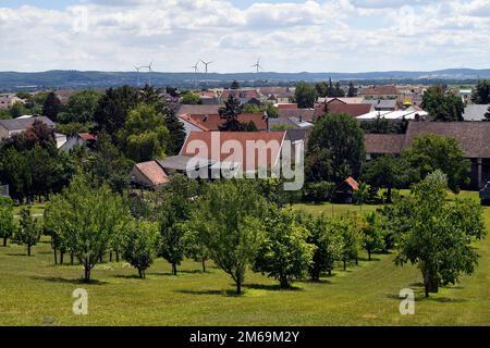 Österreich, Blick auf ein kleines Dorf in ländlicher Umgebung mit einem kleinen Obstgarten und Windturbinen im Hintergrund Stockfoto