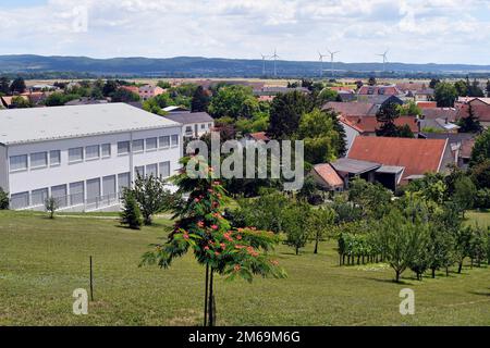 Österreich, Blick auf ein kleines Dorf in ländlicher Umgebung mit einem kleinen Obstgarten und Windturbinen im Hintergrund Stockfoto