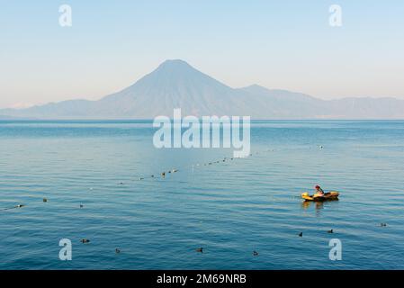 Einheimischer Maya-Fischer auf dem Atitlan-See bei Panajachel mit Vulkan im Hintergrund, Guatemala. Stockfoto