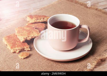 Eine Tasse Tee und hausgemachte Kekse auf sacktuchiger Serviette auf einem Holztisch, Nahaufnahme. Stockfoto