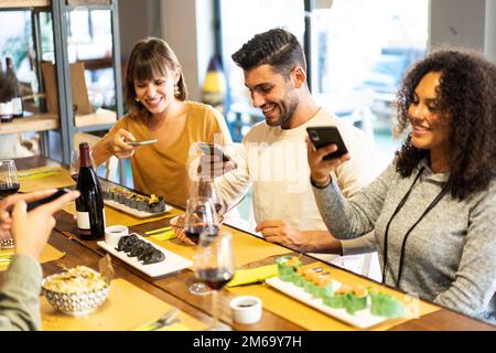 Multikulturelle, trendige Freunde fotografieren Fusion Food mit Smartphone in der Fusion Restaurant Bar - Essen und Trinken Lifestyle Konzept mit fröhlichem Youn Stockfoto