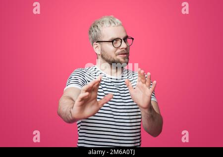 Bärtiger Mann, der sich vor plötzlicher Angst die Hände hebt, stoppt, lehnt sich ab, sieht verängstigt aus, isoliert auf rosa Hintergrund. Isoliertes Porträt Stockfoto