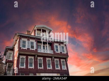 Großes Holzhaus im Hintergrund des roten Himmels bei Sonnenuntergang. Großes Holzhaus und roter, wolkiger Himmel, Kopierraum, leer. Stockfoto