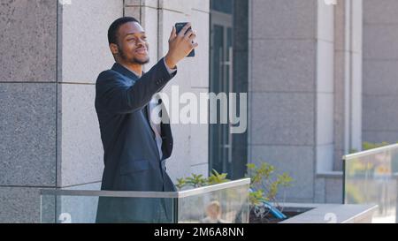 Afroamerikanischer Büroangestellter steht auf dem Balkon ethnischer Geschäftsmann Unternehmer Manager Angestellter Handy hält Telefonkonferenz Stockfoto