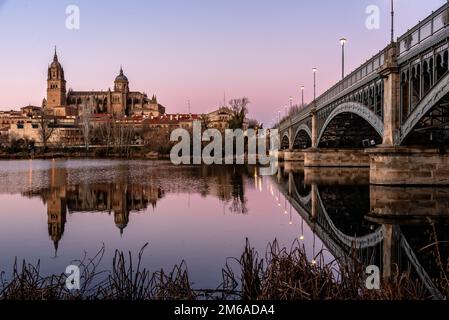 Malerischer Blick auf Salamanca mit der Kathedrale und der Eisenbrücke, die sich bei Sonnenuntergang im Fluss Tormes widerspiegeln. Castilla Leon, Spanien Stockfoto