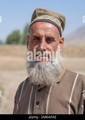 In der Nähe von Kulob, Khatlon, Tadschikistan - 08 21 2019 : Porträt eines bärtigen tadschikischen Bauern mittleren Alters mit traditioneller ethnischer Schädelmütze auf seinem Feld Stockfoto