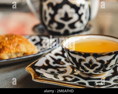 Frisches, heißes Brötchen und eine Tasse duftender Tee. Sonniger, klarer Tag. Nahaufnahme, draußen, keine Menschen. Konzept für leckere und gesunde Speisen Stockfoto